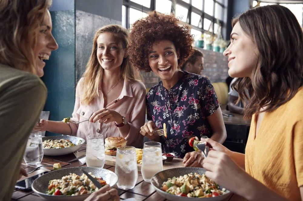 Clientes partageant un repas autour d'une table de restaurant avec salades, burger et verres d'eau