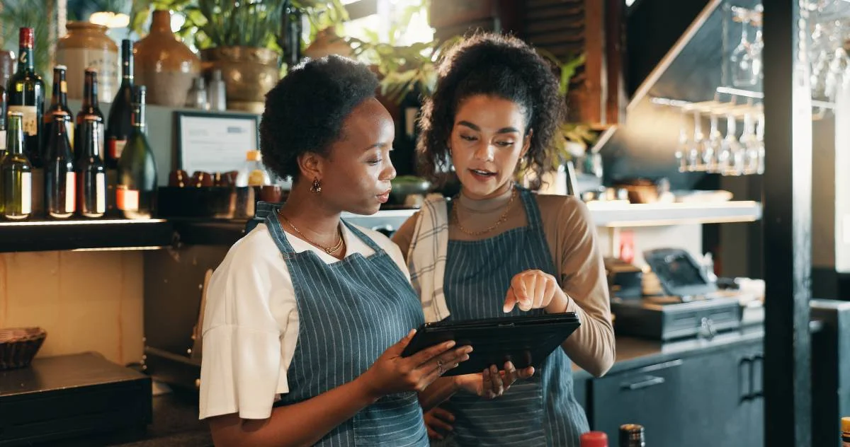 Deux serveuses en tablier consultant une tablette derrière le comptoir d'un restaurant